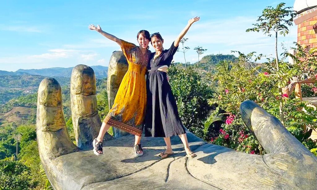 シラオガーデンの手のモニュメント上で写真撮影する女性2人